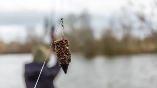 Method feeder gevuld met voermix hangend aan een vislijn met water op de achtergrond
