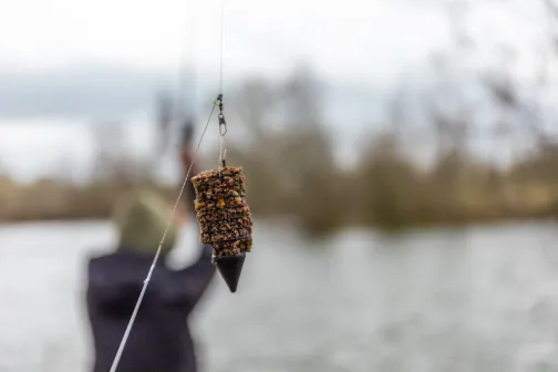 Method feeder gevuld met voermix hangend aan een vislijn met water op de achtergrond