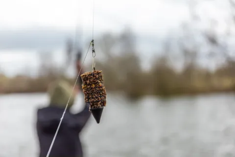 Method feeder gevuld met voermix hangend aan een vislijn met water op de achtergrond